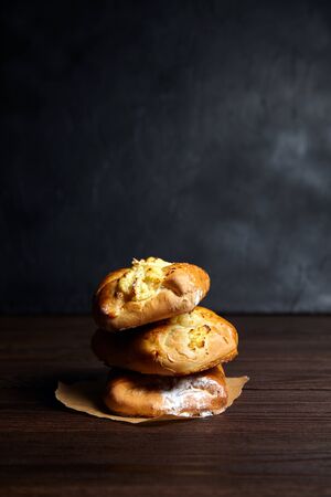 Wheat buns with curd filling on a wooden table, close-up. Bakery, three buns with cottage cheese stacked on baking paper on dark backgroundの写真素材
