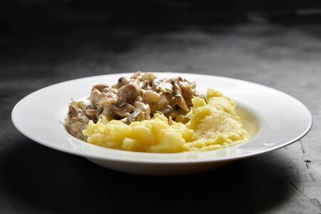 Mashed potatoes with fried oyster mushrooms in a white ceramic plate on a black stone tableの写真素材
