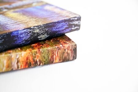 Photography canvas prints. Stack of colorful photos with gallery wrap on white wooden table. Stretched photo canvases, lateral side, closeupの写真素材