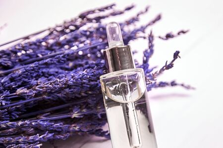 Lavender cosmetic oil in a dropper bottle with glass pepit and dried lavender flowers on white wooden background. Natural organic herbal skin care oilの写真素材
