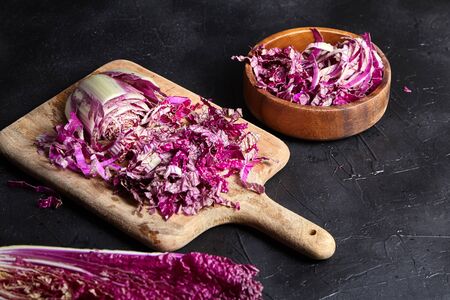 Chopped Red Chinese cabbage (Purple wombok) on wooden cutting board and bowl on stone table. Red Napa cabbage with vibrant colored leaves on black background. Cooking vegetable salad, healthy foodの写真素材