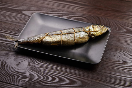 Hot smoked fish, kippered herring. Twine tied fish on black plate on brown wooden table