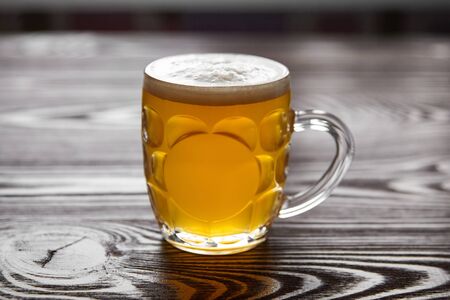 Mug of unfiltered light wheat beer on brown wooden table. Foamy white unfiltered beer in a transparent glass mug, selective focusの写真素材