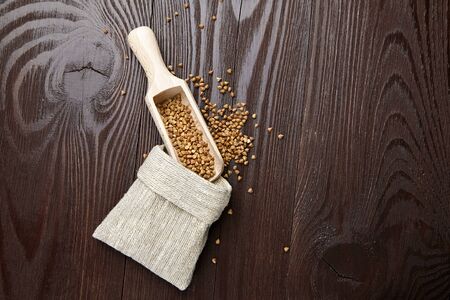 Buckwheat groats (hulled seeds) in burlap bag, scoop on wooden background, top view. Buckwheat whole grains on brown tableの写真素材