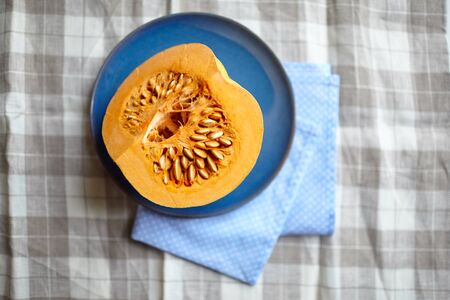 Pumpkin half on a blue plate on a table, top view. Fresh piece of pumpkin with seeds, vegetable ingredient, selective focusの写真素材