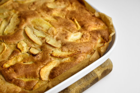 Apple pie, dessert from stewed fruits in ceramic dish for baking in the oven, closeup. Charlotte on wooden cutting board on white backgroundの写真素材