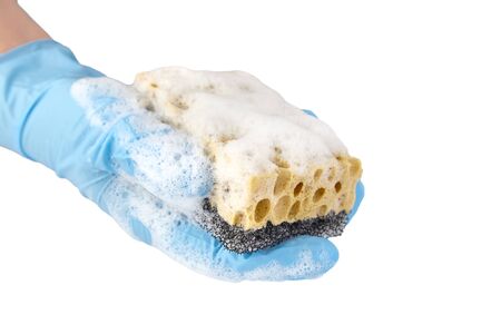 Household sponge from reticulated foam isolated on white background. Hand in blue nitrile glove holding yellow black sponge for washing dishes with detergent foamの写真素材