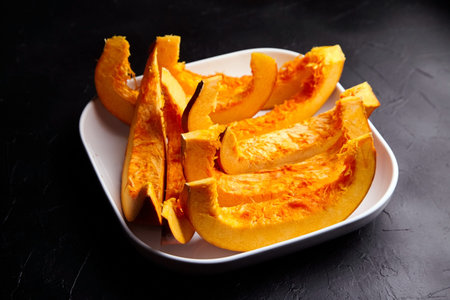 Slices of uncooked pumpkin in white ceramic plate on black stone background, selective focus. Vegetable dish, vegan diet, healthy foodの写真素材
