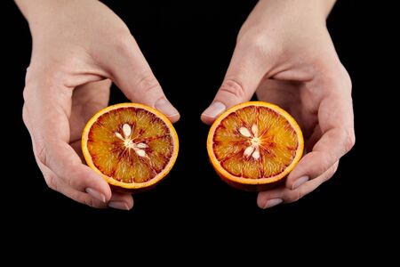 Blood or red orange fruit halves in hands on black background. Person holding halved ripe citrus fruit with red juicy flesh, selective focusの写真素材