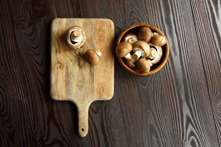 Mushrooms on cutting board, many fresh brown champignons in bowl on a wooden background, top view. Uncooked food ingredient, flat layの写真素材