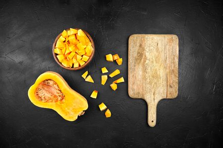 Pumpkin pieces, half of butternut squash, wooden bowl with chopped pumpkin, cutting board on black background, top view, flat layの写真素材