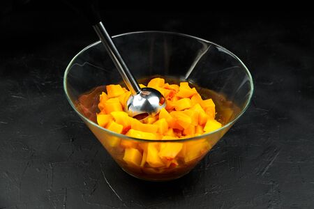 Pumpkin pieces and blender in a glass bowl on black table. Chopped butternut squash in salad dish. Cooking vegetable food, pumpkin puree (mash) recipeの写真素材