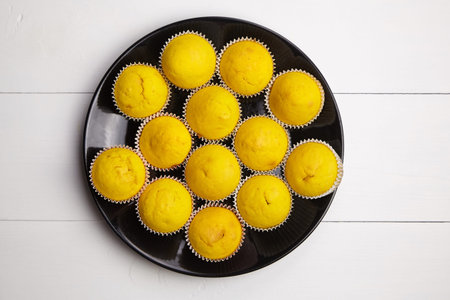Pumpkin muffins on black plate on wooden table, flat lay. Vegetable cupcakes on white background....