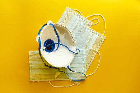 Respirator and surgical masks on yellow background. Disposable medical face masks. Airborne disease...