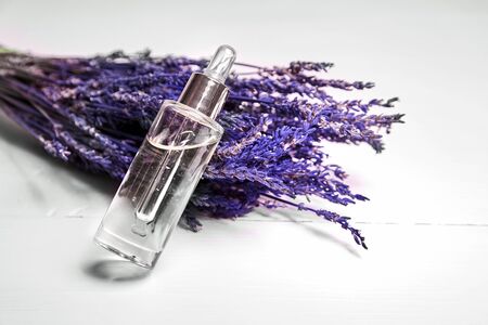 Lavender cosmetic oil in a dropper bottle with glass pepit and dried lavender flowers on white wooden background. Natural organic herbal skin care oilの写真素材
