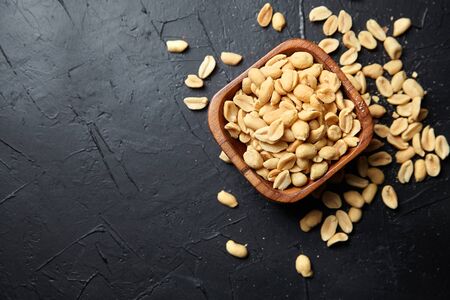 Wooden bowl with roasted peeled peanuts, salty beer snack on dark background with copy space, top viewの写真素材
