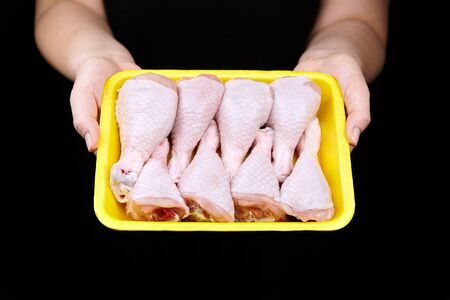 Chicken shin in yellow tray on black background. Woman holds box with fresh chicken legs. Female hands, raw poultry meatの写真素材