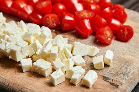 Fresh red cherry tomatoes with salad cheese on wooden cutting board, closeup. Cooking vegetable saladの写真素材