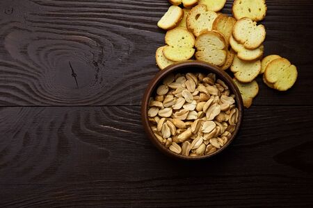 Bruschette chips, dry slices of baked bread, roasted peanut peeled in a bowl, beer snacks on wooden background, top viewの写真素材