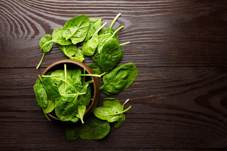 Spinach fresh green leaves in a bowl on wooden background, top view. Healthy food, salad dish,...