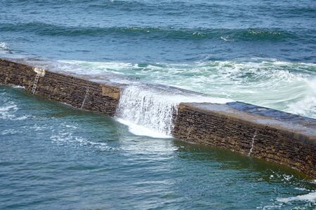 Dike and ocean waves with white foam. Digue de Sainte-Barbe in Saint Jean de Luz, France. The waters of the Bay of Biscay. Splashing sea water. Engineering structure for protection against sea wavesの写真素材