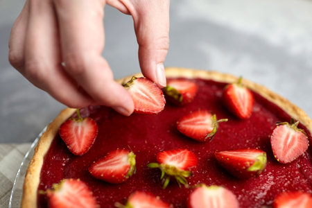 Strawberry tart decoration. Hand accurately puts a half of a berry on top of red berry tart.