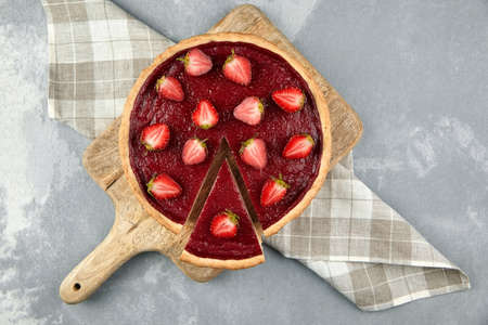 Strawberry pie with fresh berries halves on gray stone background. Sweet summer desser on wooden cutting board, top view. Piece of pie, napkin. flat layの写真素材
