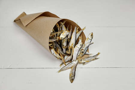 Small salted dried fish in paper bag on white wooden table background. Beer appetizer.の写真素材