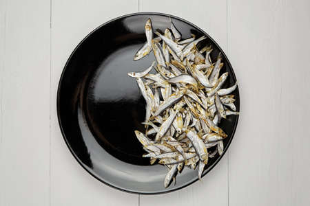Small salted stockfish heap in black plate on white wooden table background.の写真素材