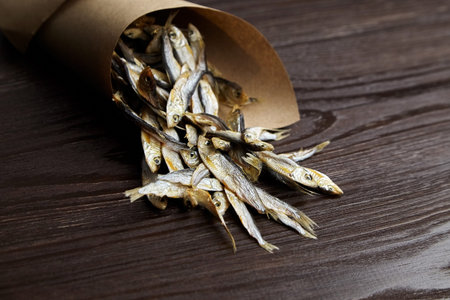 Sun-dried salty small fish. Stockfish in paper bag on dark wooden background.