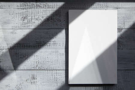 White blank canvas hangs on gray wooden wall with a shadow from the sunlight covering. Mockup, front view, copy spaceの写真素材
