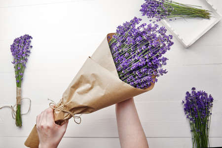 Beautiful natural lavender flowers bouquet wrapped in paper in woman hands over white wooden backgroundの写真素材
