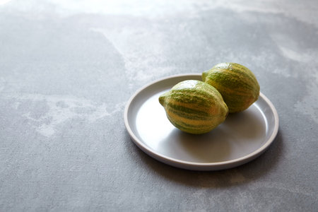 Two variegated pink lemons with green-striped rind in gray plate on concrete background with copy...