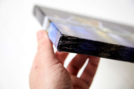 Canvas print. Hand holds a photo with gallery wrap method of canvas stretching on stretcher bar. Sample of stretched color photograph printed on canvas, lateral side, closeup.の写真素材