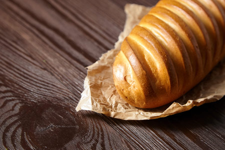 Bakery product. Baked whole bun on wooden table. Loaf, white wheat bread on baking paper on brown...