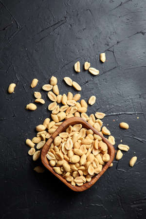Wooden bowl with roasted peeled peanuts, salty beer snack on dark background with copy space, top viewの写真素材