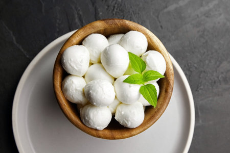Mini mozzarella cheese balls in wooden plate on black stony background, top view. Traditional...