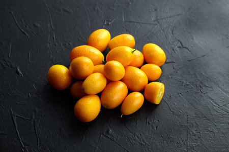 Kumquat, fresh citrus fruits, Nagami variety. Heap of ripe cumquats on black table, closeup,...