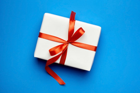White gift box tied with red ribbon on blue background