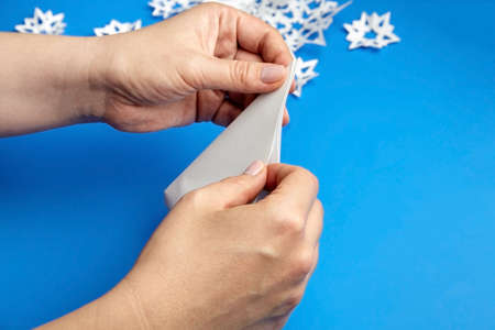 Hands making white paper snowflakes over blue backgroundの写真素材