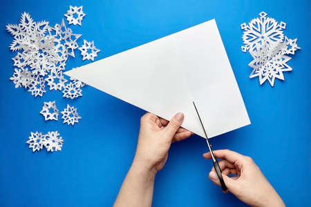 Hands cutting a sheet of white paper for making snowflakesの写真素材