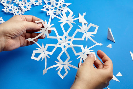 Hands holding white cutted paper snowflake on blue surfaceの写真素材