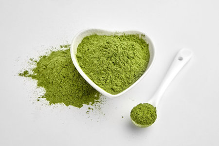 Organic wheatgrass or barley grass powder in ceramic bowl and spoon on white. Detox superfood...