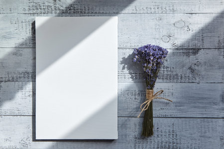 White blank canvas and bouquet of lavender flowers on wooden table with a shadow from the sunlight...