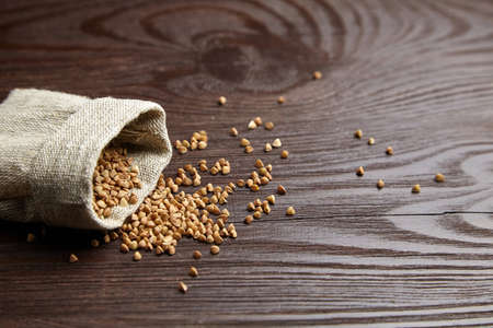 Buckwheat groats (hulled seeds) in burlap bag. Buckwheat whole grains scattered on wooden background with copy space, selective focusの写真素材