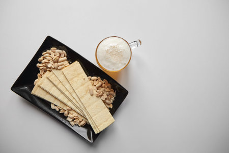 Mug of unfiltered light wheat beer with beer snacks on white table, top view. White unfiltered beer,...
