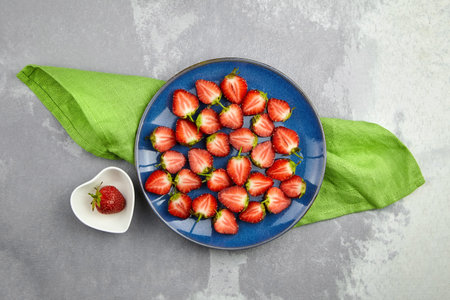 Ripe red strawberries cut in half on blue and white ceramic plates flat lay on gray concrete table background.の写真素材