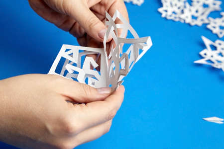 Hands holding white cutted paper snowflake on blue surfaceの写真素材