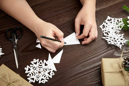 Hands making white paper snowflakes over wooden tableの写真素材