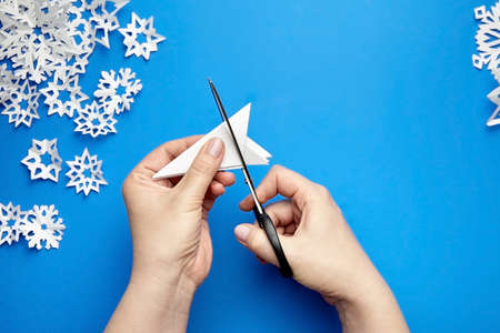 Hands cutting white paper snowflakes over blue backgroundの写真素材
